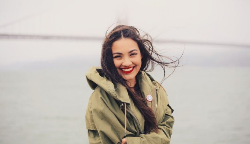 A woman in a green jacket is smiling in front of the golden gate bridge.