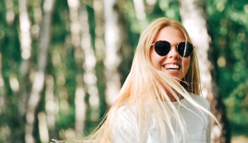A young blonde woman wearing sunglasses in a forest.