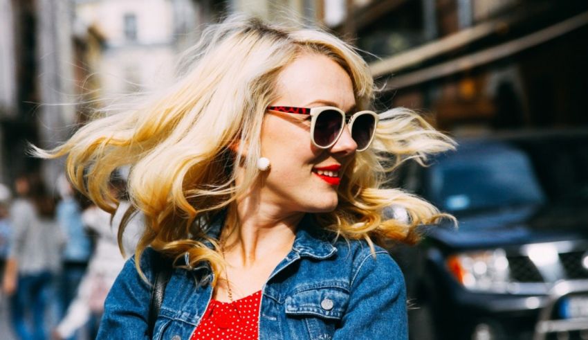 A woman wearing sunglasses and a denim jacket on a city street.