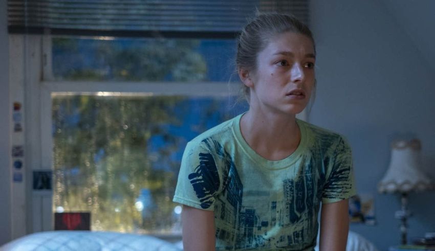 A young girl in a green shirt sitting on a bed.