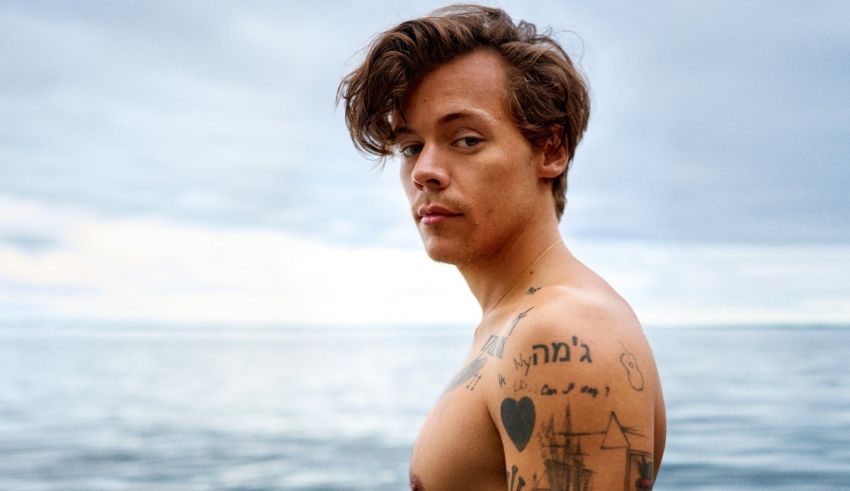 A man with tattoos standing by the ocean.