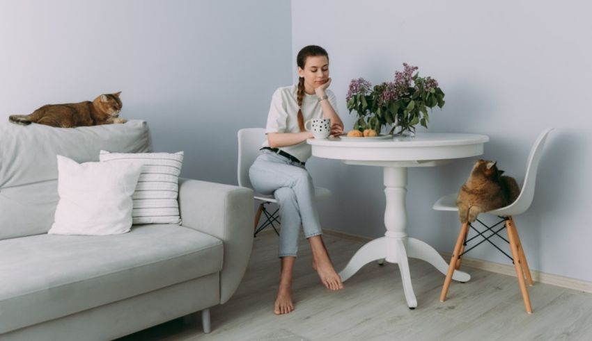 A young woman sitting at a table with cats and plants.