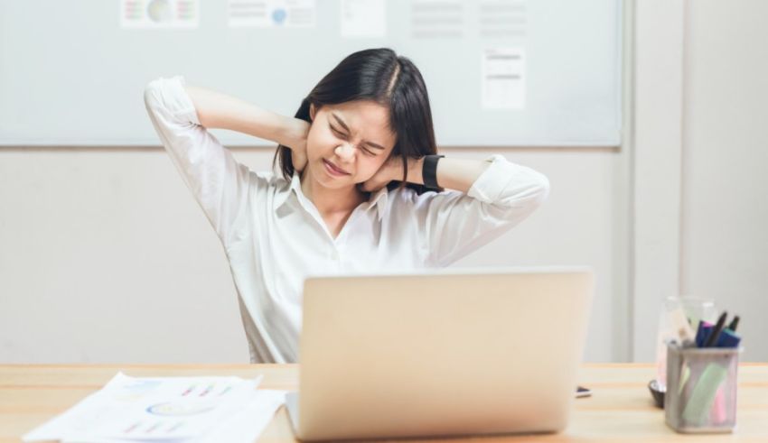 An asian woman is sitting at a desk with her hands on her head.