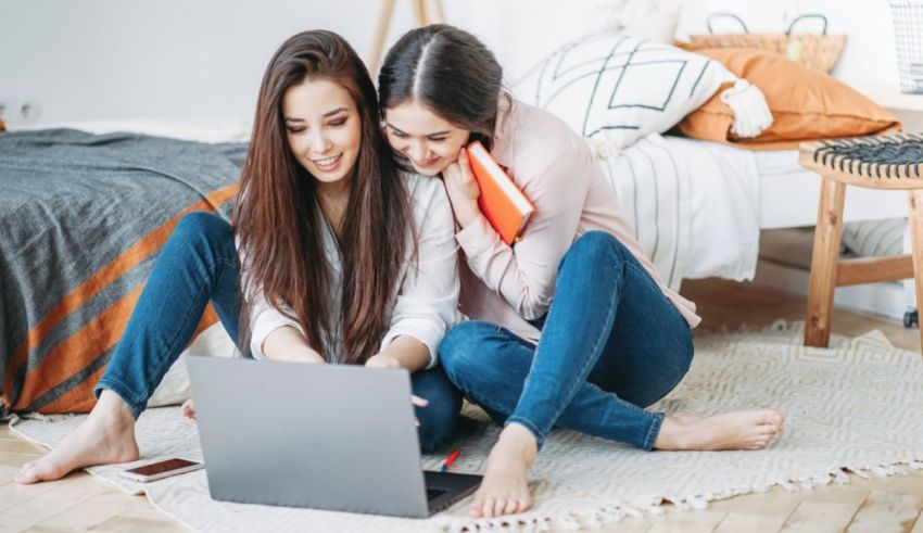 Two young women sitting on the floor and using a laptop.