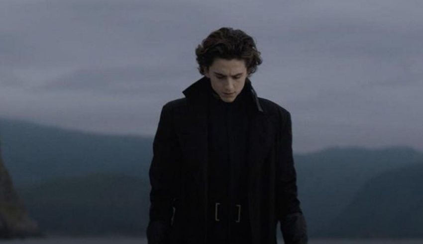 A man in a black coat standing in front of a body of water.