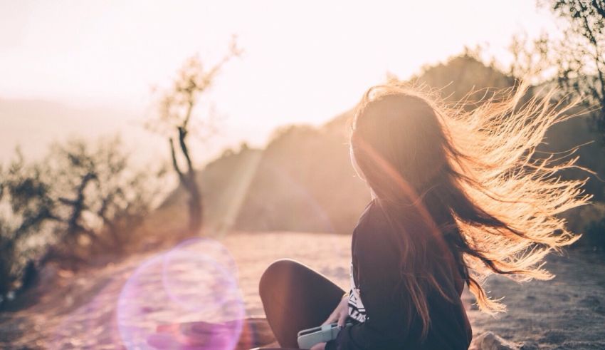 A woman sitting on a hill with her hair blowing in the wind.