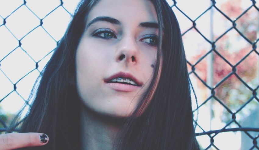 A girl with long hair standing behind a chain link fence.