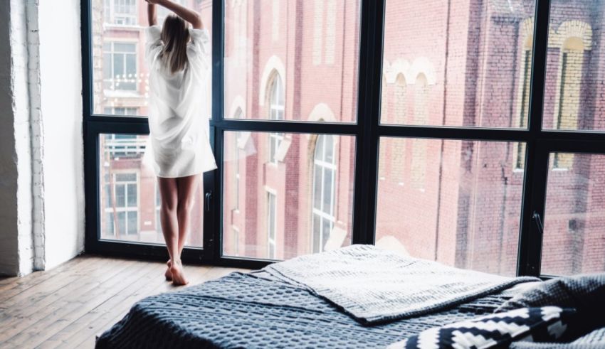 A woman standing in front of a large window in a bedroom.