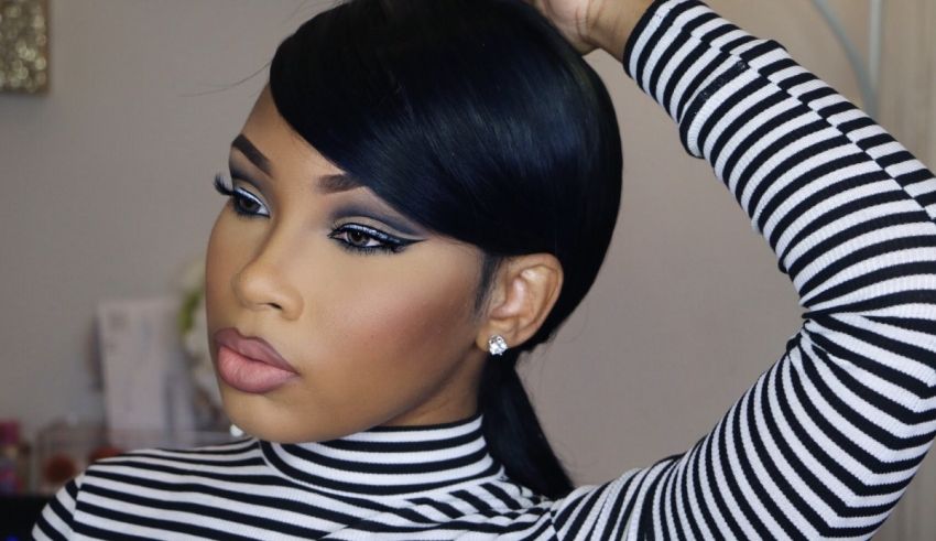 A black woman is putting her hair up in a ponytail.