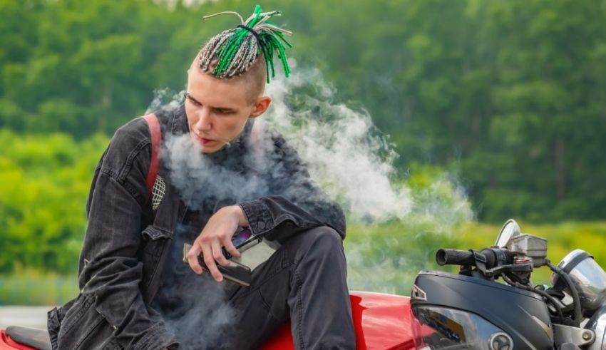 A young man smoking a cigarette on a motorcycle.