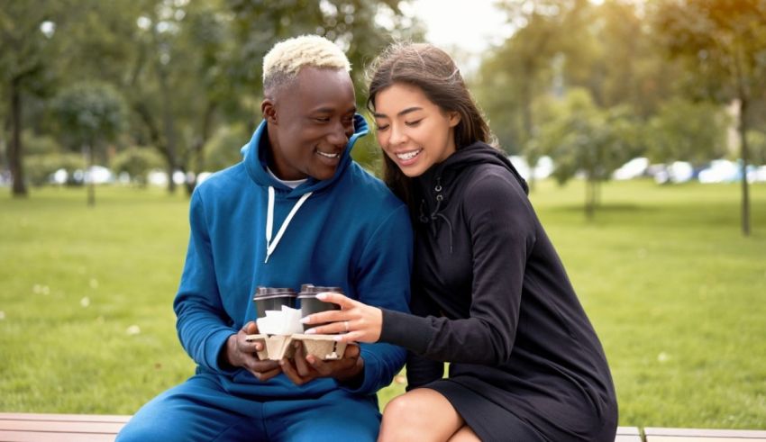 A young man and woman sitting on a bench in a park.