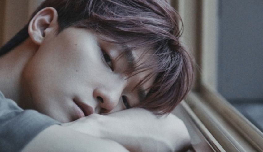 A young man is laying on a window sill.