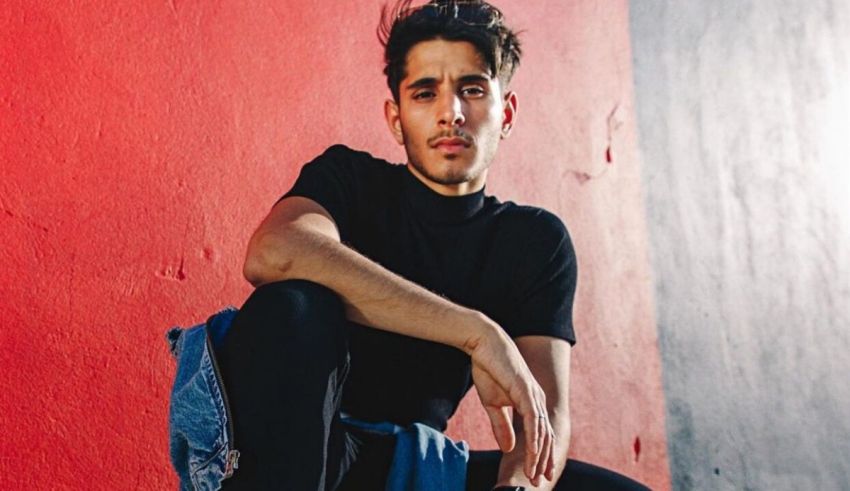 A young man sitting on a red wall.