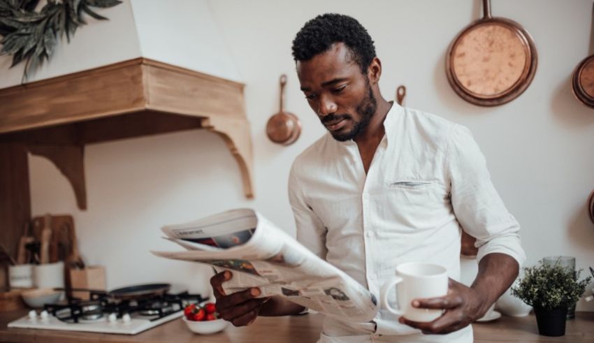A man reading a newspaper in the kitchen.