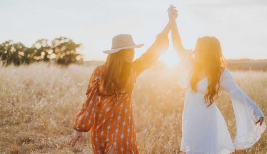Two women holding hands in a field at sunset.