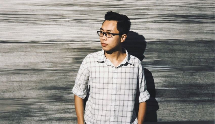 A man in glasses is leaning against a wall.