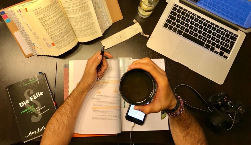 A man writing on a desk with a laptop and a cup of coffee.