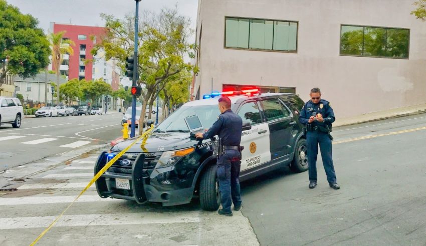 Two police officers standing next to a police car on a street.
