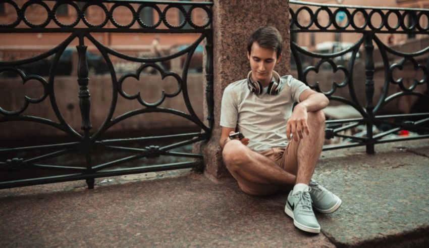 A young man sitting on a railing in front of a bridge.