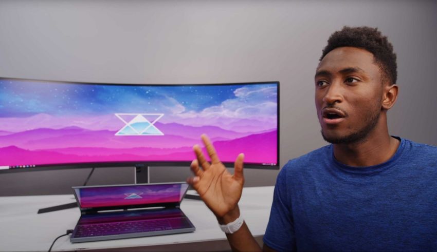 A man is standing in front of a laptop and a monitor.