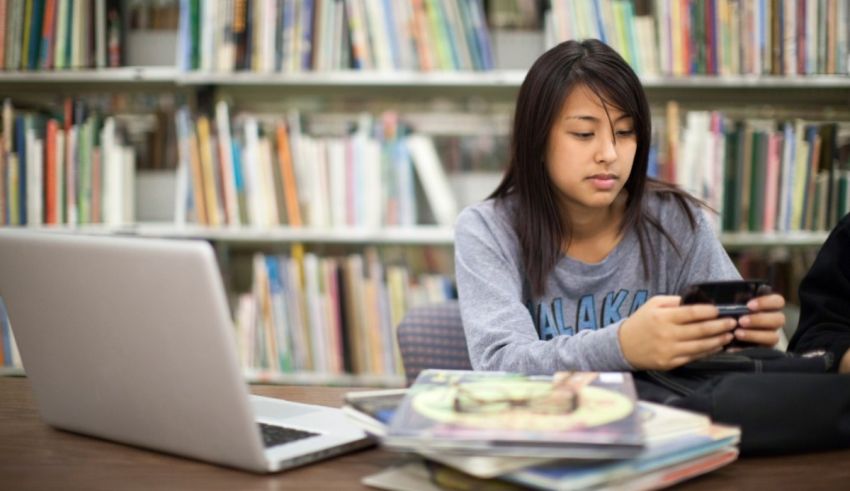 Two girls sitting at a table with a laptop and cell phone.