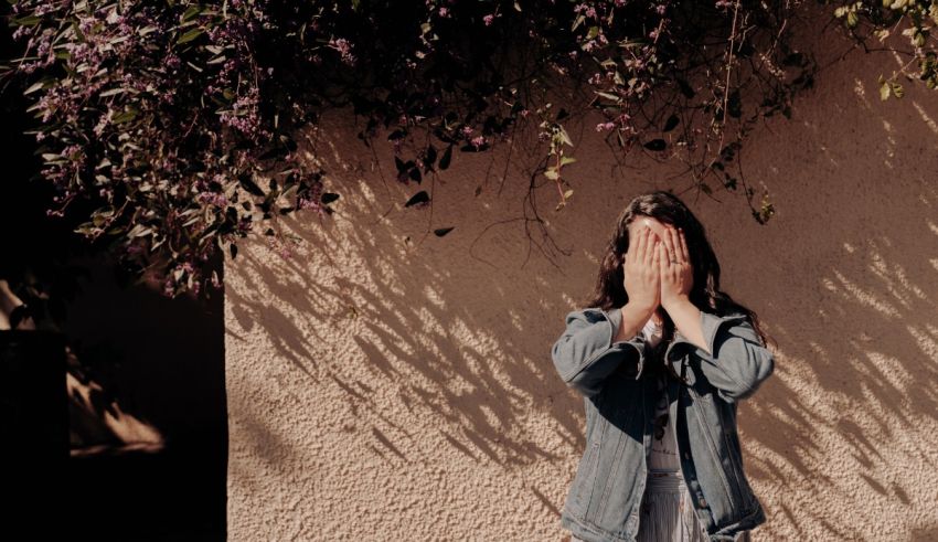 A woman with her hands covering her face in front of a wall.