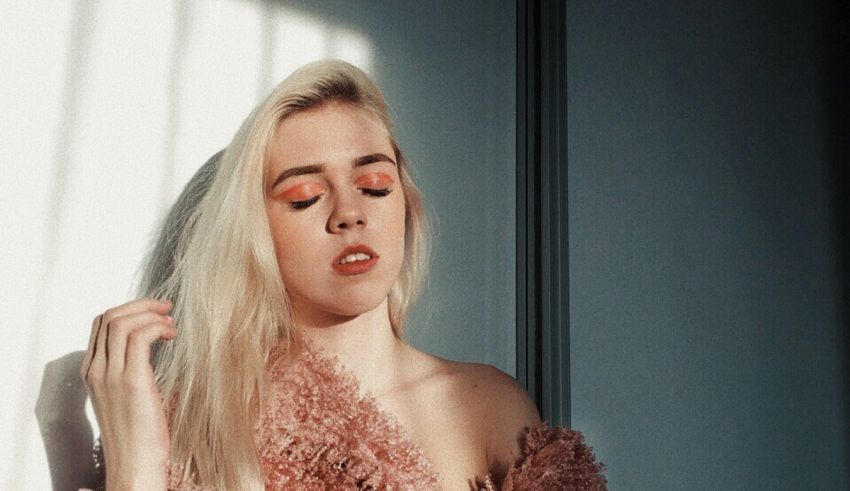 A woman in a pink sweater leaning against a wall.
