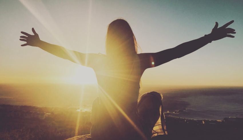 A woman sitting on top of a mountain with her arms outstretched.