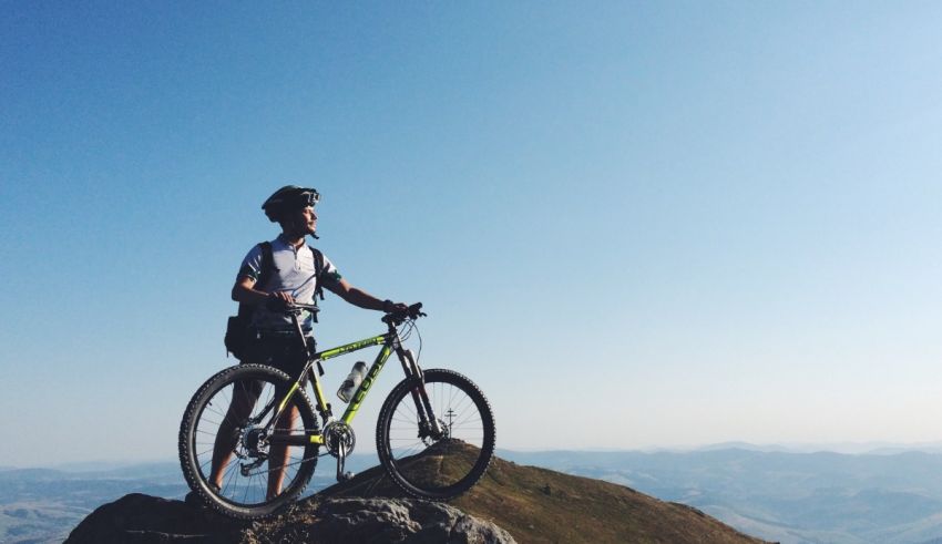 A man standing on top of a mountain with his mountain bike.