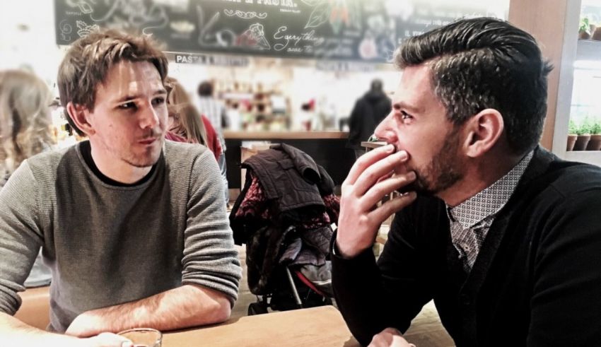 Two men sitting at a table talking to each other.