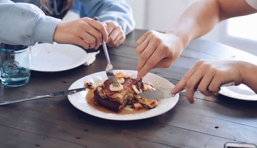 Two people eating pancakes with forks on a table.