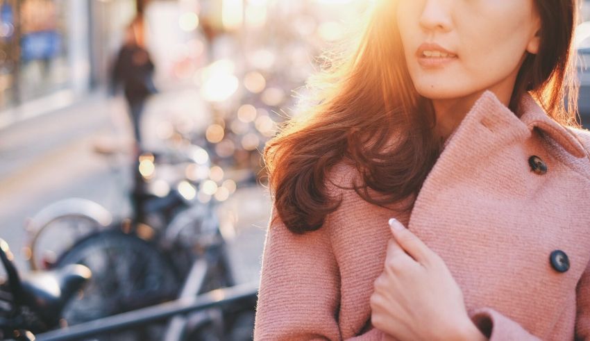 A woman in a pink coat is standing on a street.