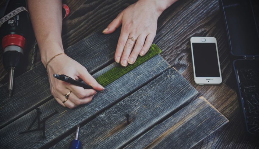 A woman is working on a piece of wood with a pen and a cell phone.