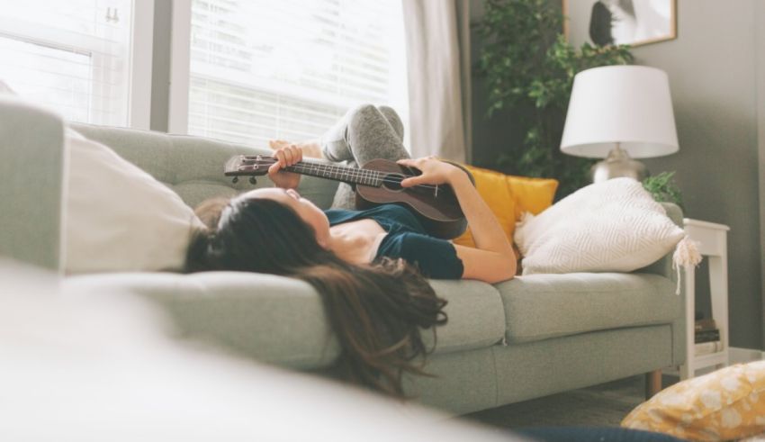 A woman laying on a couch playing an ukulele.