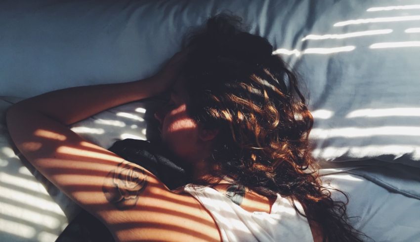 A woman laying in bed with a sun hat on her head.