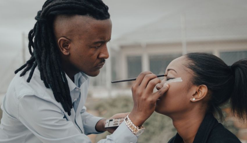 A man with dreadlocks is applying makeup to a woman.