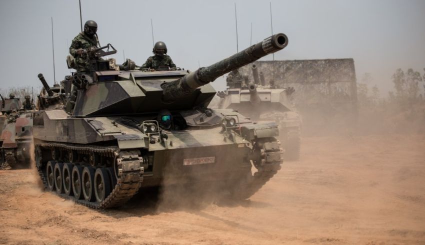 A group of soldiers are driving a tank on a dirt field.