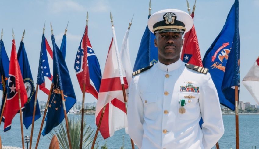 A navy officer standing in front of flags.