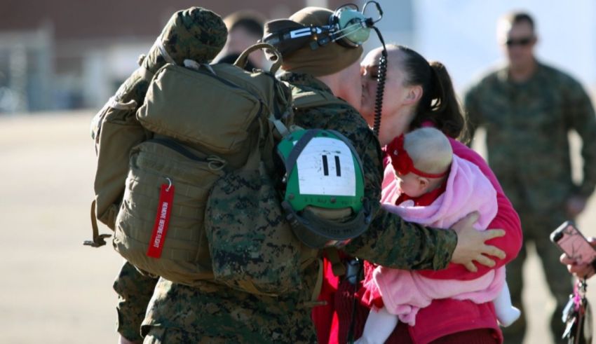 A military man is hugging a baby in front of a group of people.