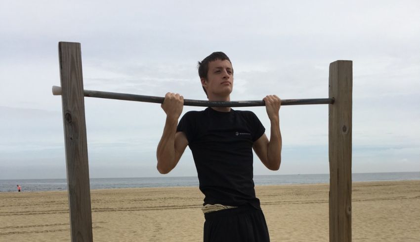 A man doing pull ups on a bar at the beach.