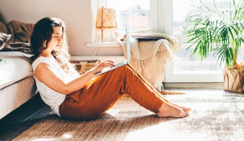 A woman sitting on the floor with her laptop in front of a window.