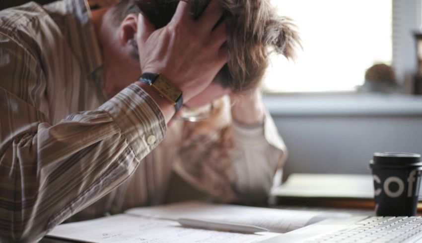 A man is sitting at his desk with his hands on his head.