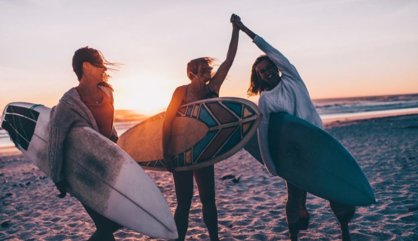 Three women holding surfboards on the beach at sunset.