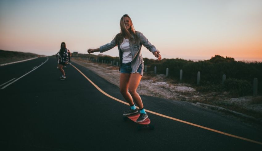 Two girls riding skateboards on a road at sunset.