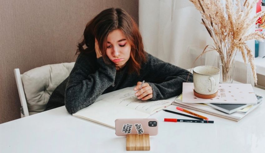 A girl sitting at a desk with a phone and a plant.