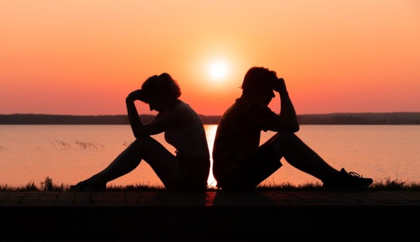 Two people sitting on a bench near a lake at sunset.