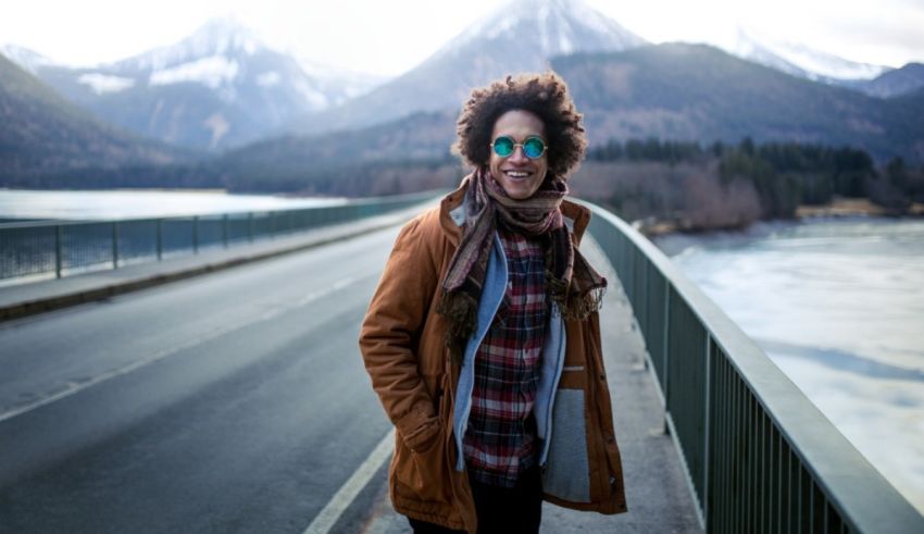 A young man standing on a bridge with mountains in the background.