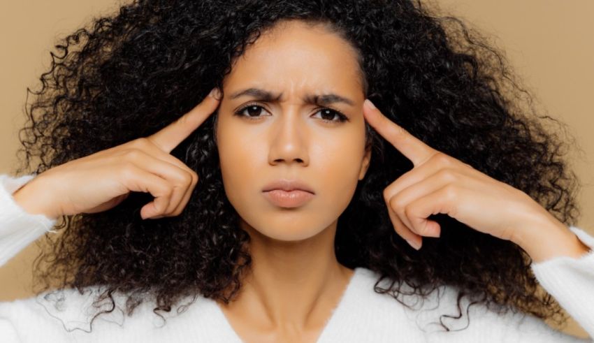 A woman with curly hair covering her eyes with her hands.