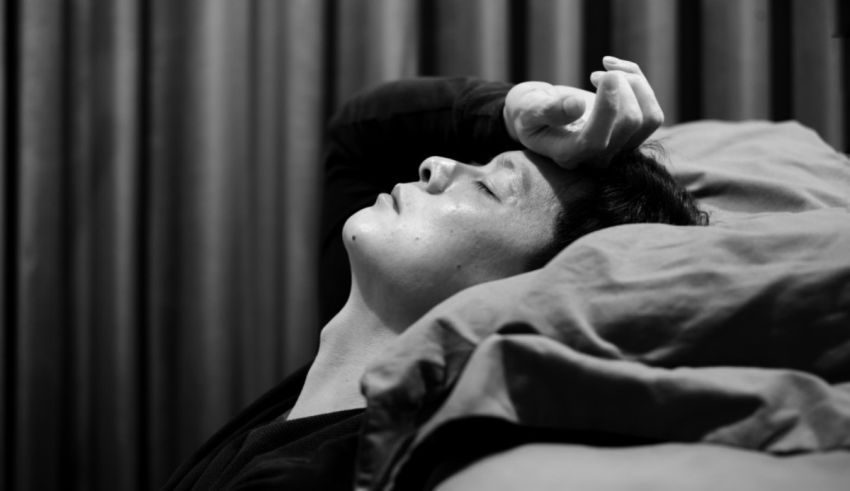 A man laying in bed with his hand on his head.