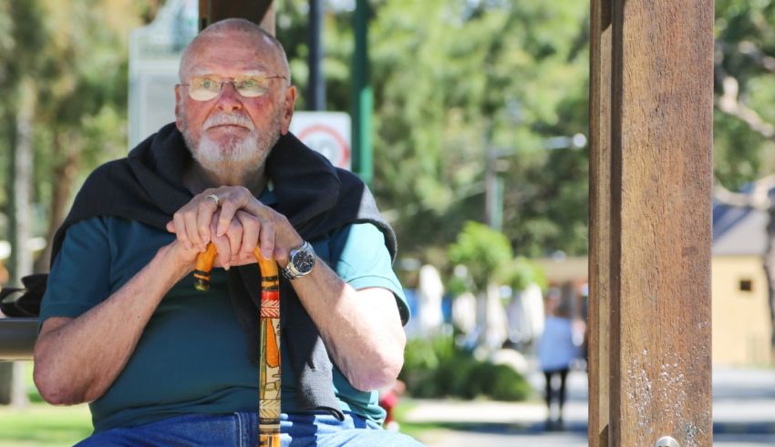 An older man sitting on a bench with a cane.